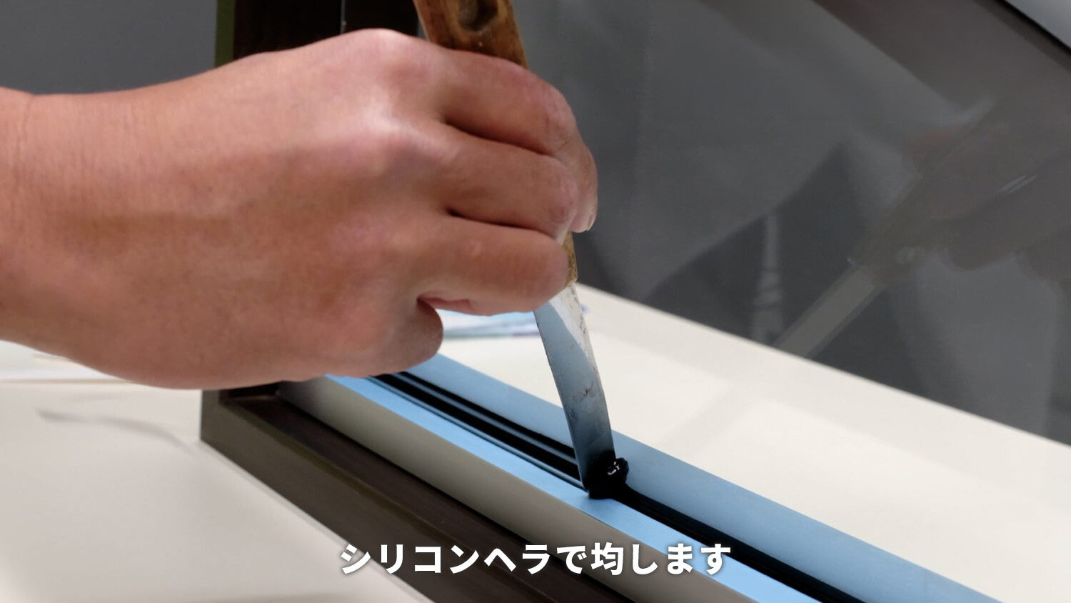 ガラス屋がコーキングする際にシリコンヘラで均している状態